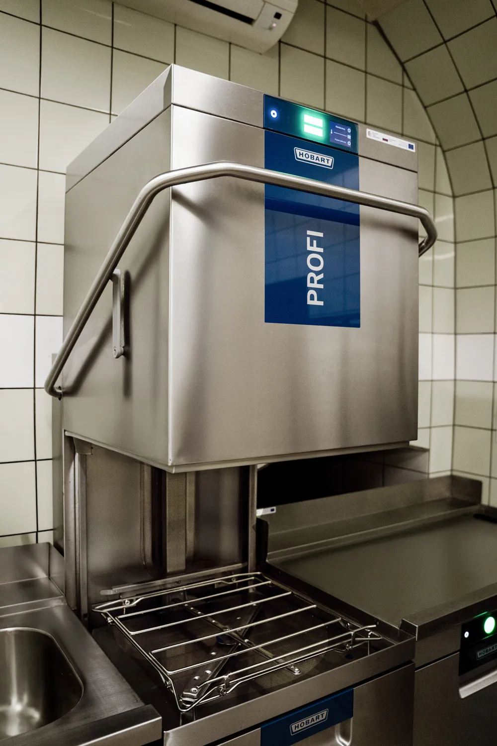 Profesjonalna zmywarka gastronomiczna kapturowa Hobart PROFI ze stali nierdzewnej, z otwartą komorą i panelem sterowania w kuchni restauracyjnej.