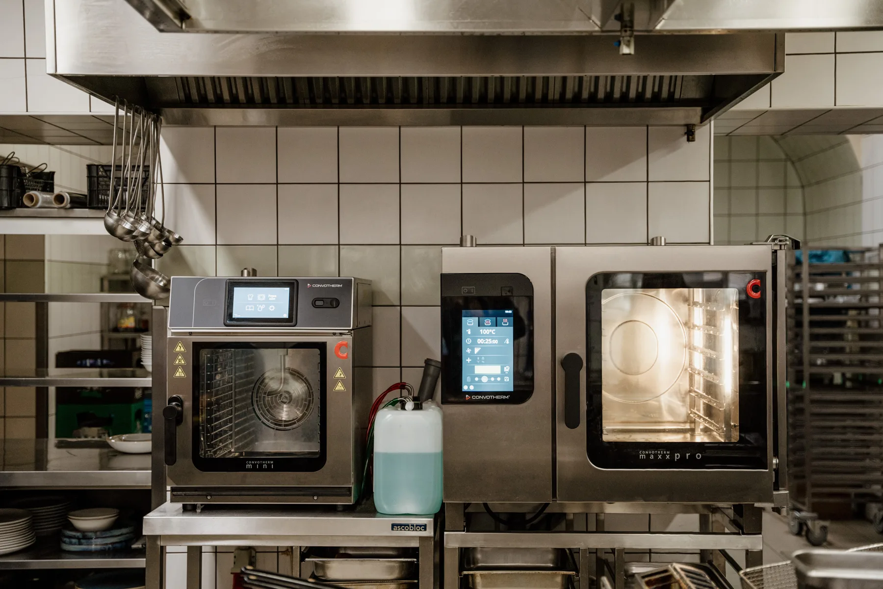 Profesjonalne piece konwekcyjno-parowe w kuchni gastronomicznej, ustawione pod okapem, z dotykowymi panelami sterowania i otwartą komorą pieczenia.