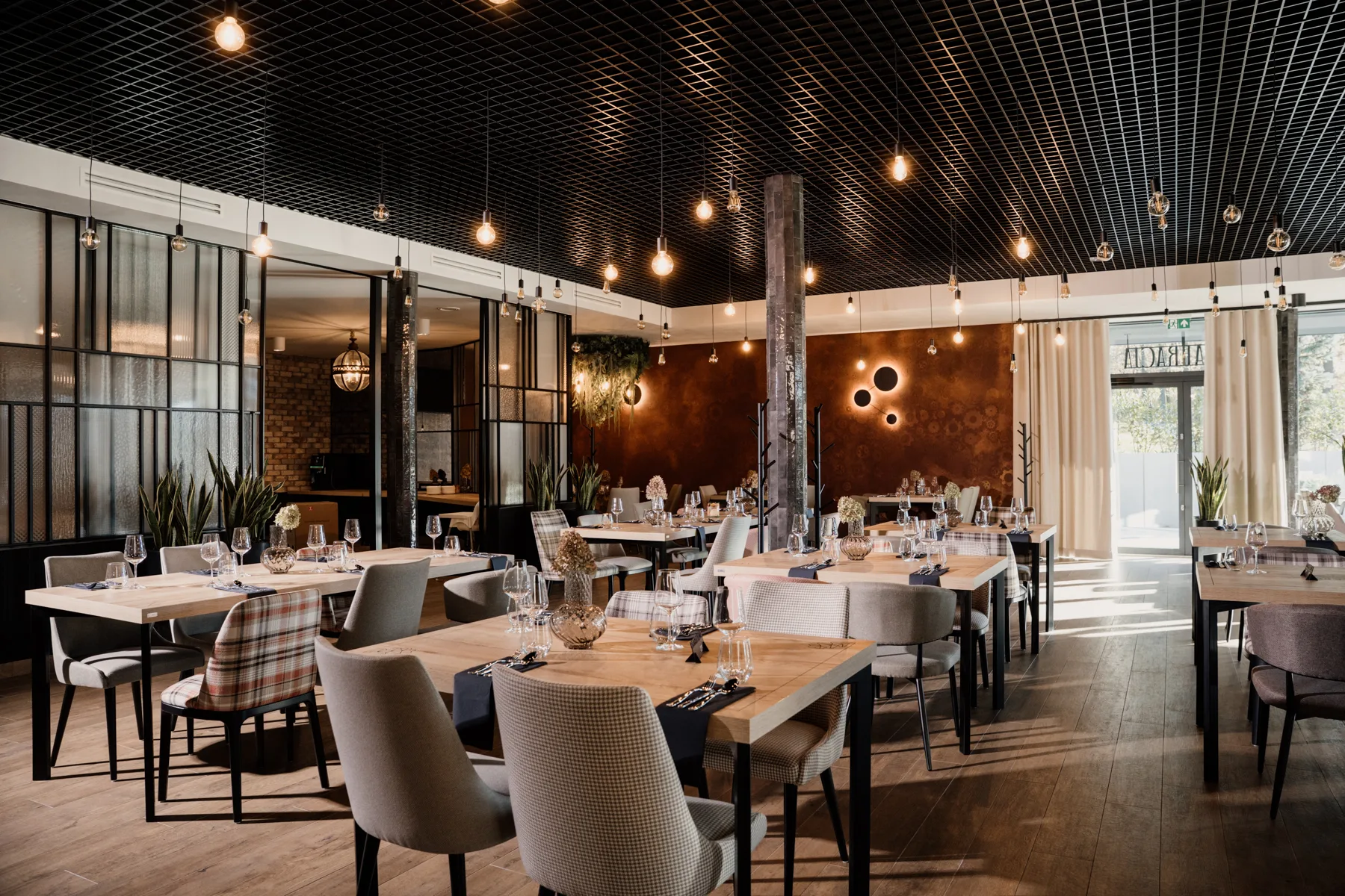 Nowoczesne wnętrze restauracji z elegancko nakrytymi stołami, designerskim oświetleniem i industrialnym sufitem, przygotowane na obsługę gości.