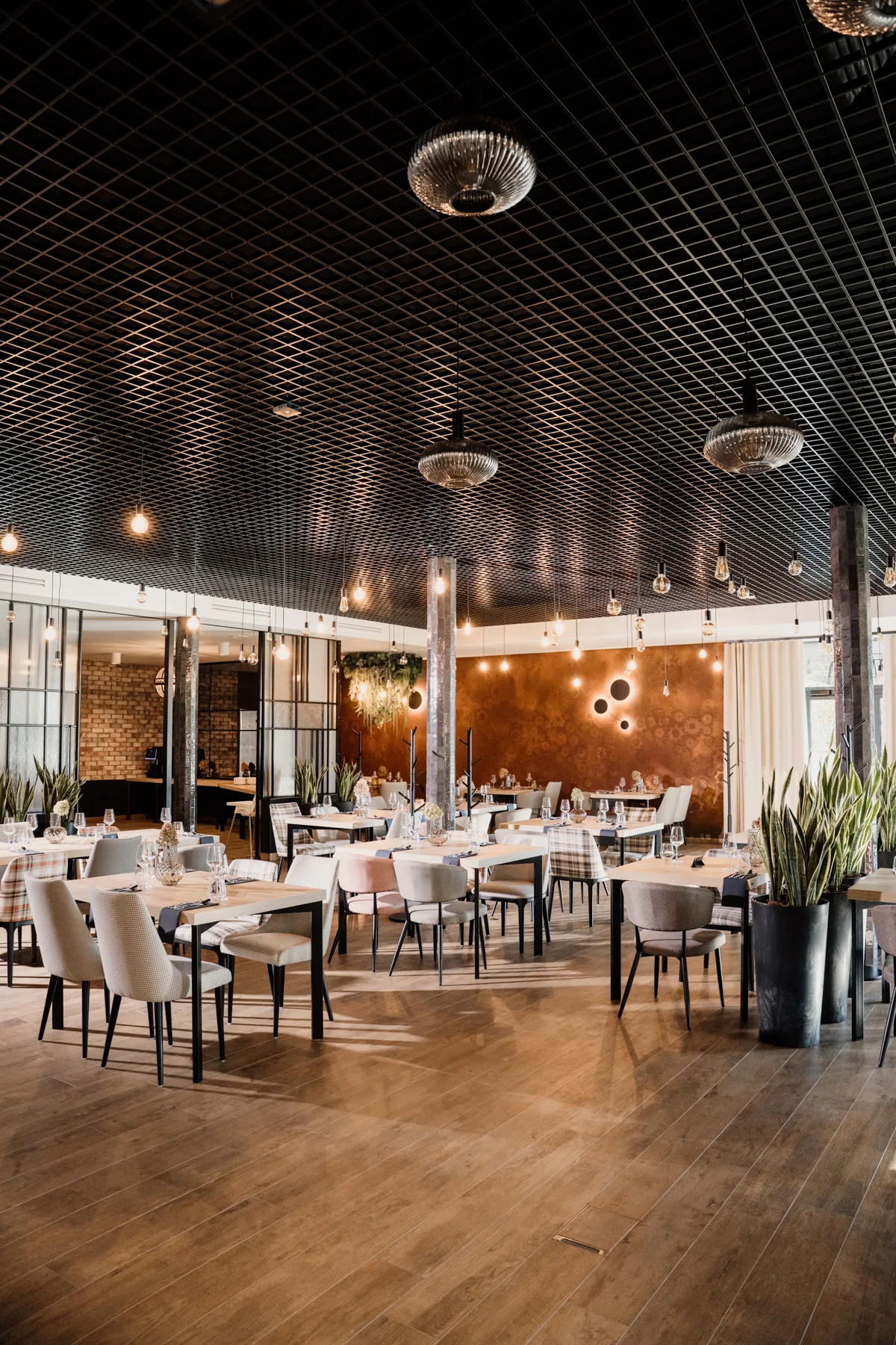 Nowoczesne wnętrze restauracji z elegancko nakrytymi stołami, designerskim oświetleniem i industrialnym sufitem, przygotowane na obsługę gości.