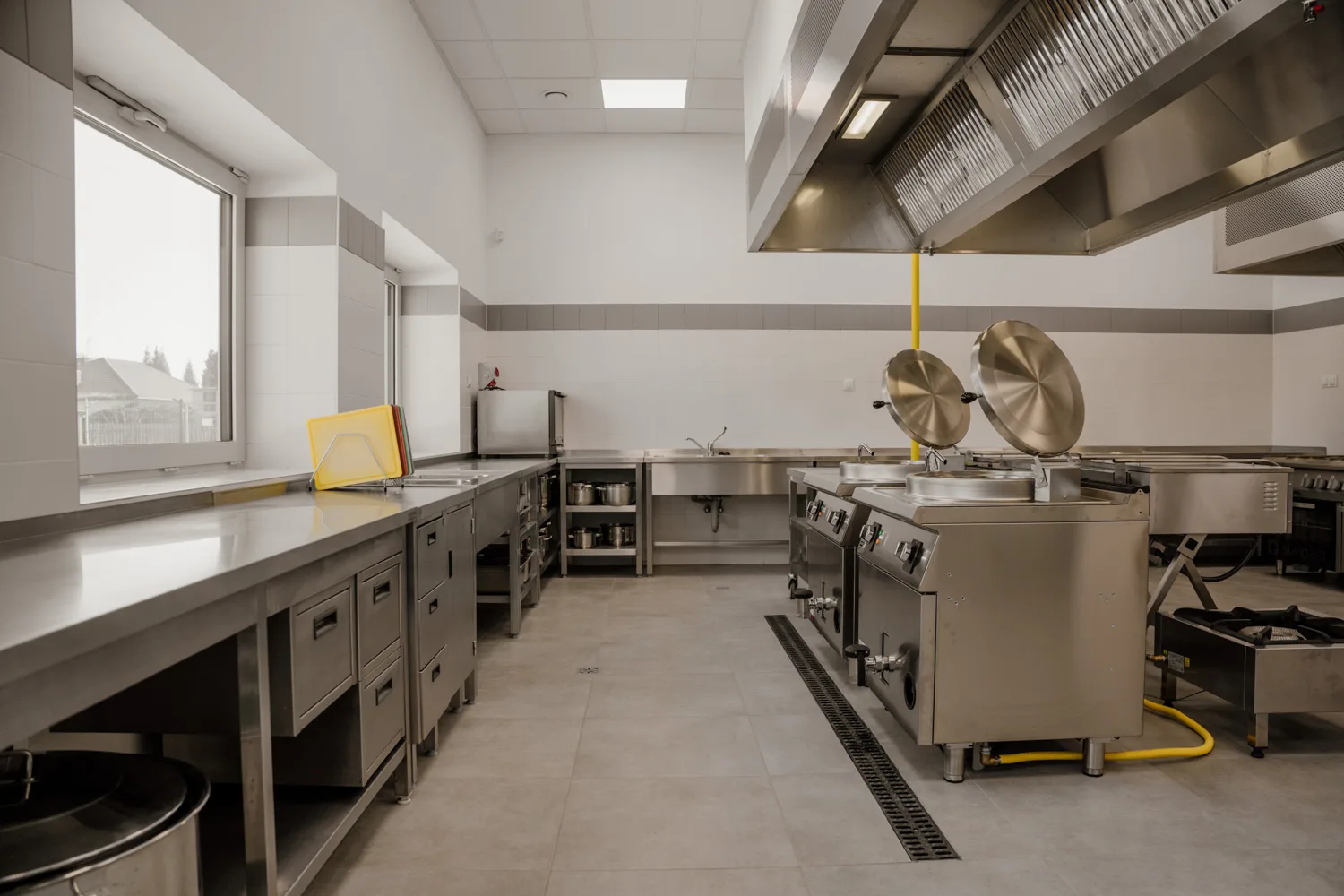 Nowoczesna kuchnia gastronomiczna ze stali nierdzewnej, wyposażona w profesjonalne urządzenia grzewcze, stoły robocze i okap przemysłowy.