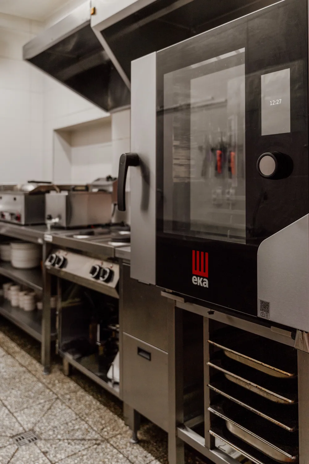 Profesjonalny piec konwekcyjno-parowy EKA w zapleczu kuchni gastronomicznej, obok linii grzewczej i okapu ze stali nierdzewnej.