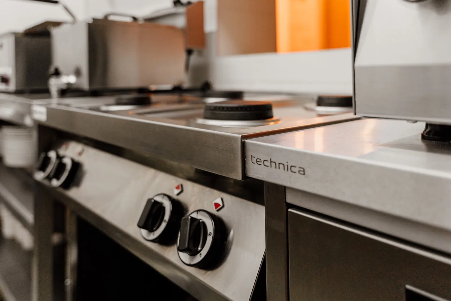 Zbliżenie na profesjonalną kuchnię gazową Technica ze stali nierdzewnej, z widocznymi palnikami i pokrętłami sterującymi.