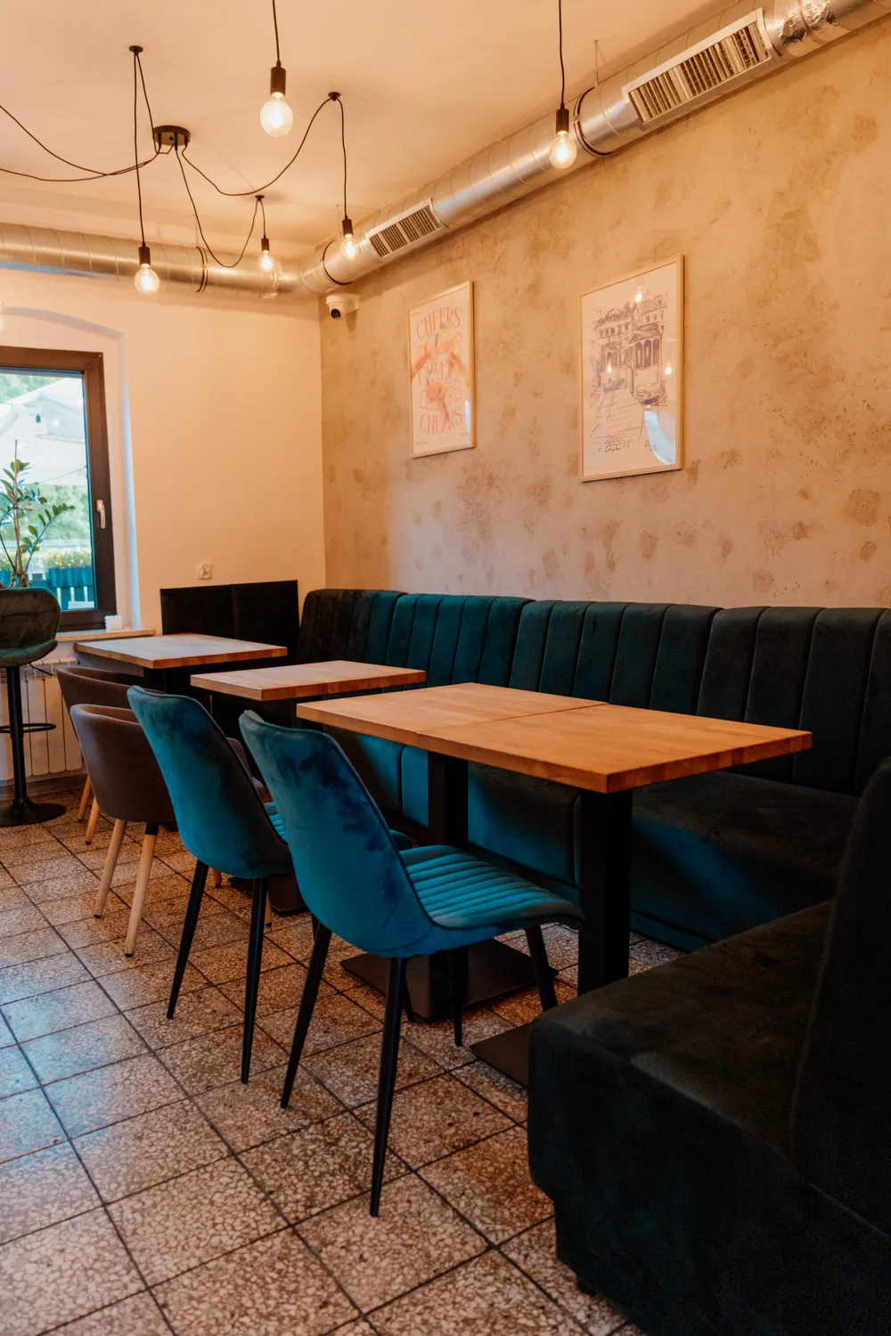Widok na salę w lokalu gastronomicznym, welurowe fotele i kanapy, drewniane stoliki.