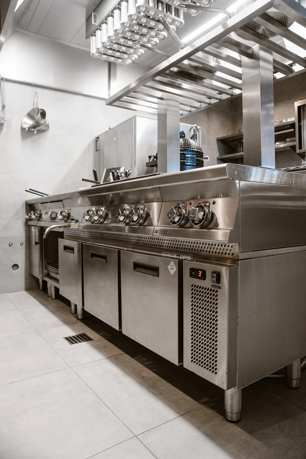 Profesjonalna kuchnia gastronomiczna ze stalową kuchnią grzewczą, okapem sufitowym, półkami roboczymi i nowoczesnym wyposażeniem ze stali nierdzewnej.