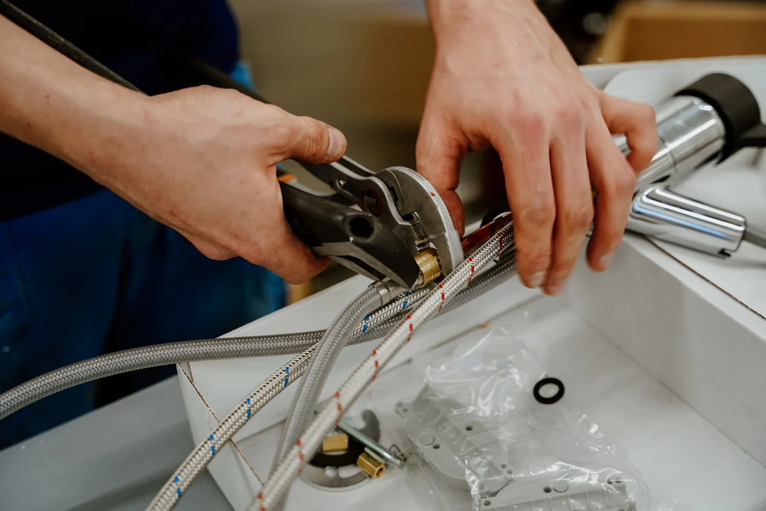 Zbliżenie na dłonie montujące baterię kuchenną – dokręcanie węży przyłączeniowych kluczem nastawnym pod zlewem.