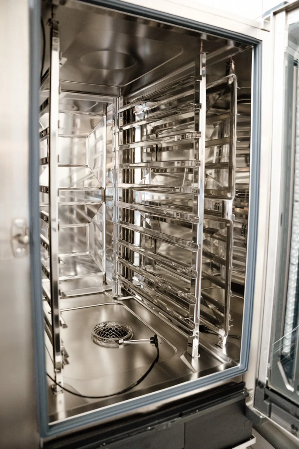 Wnętrze profesjonalnego pieca konwekcyjno-parowego ze stali nierdzewnej, z prowadnicami na blachy i systemem cyrkulacji powietrza.