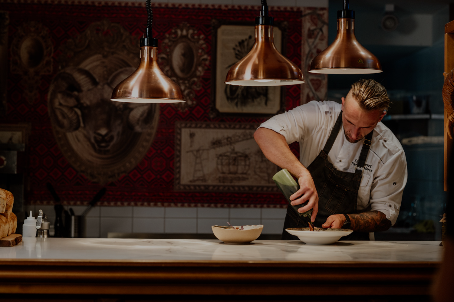 Szef kuchni wykańczający danie w restauracji typu open kitchen – precyzyjne serwowanie potrawy przy ladzie.