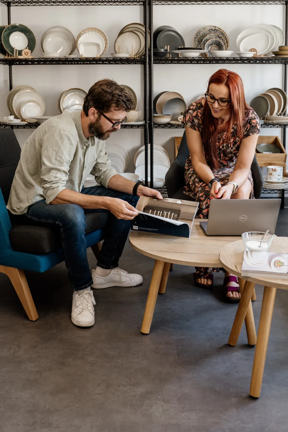 Dwójka specjalistów omawiająca projekt wyposażenia gastronomicznego – mężczyzna przegląda katalog, kobieta pracuje na laptopie w showroomie z ekspozycją porcelany.