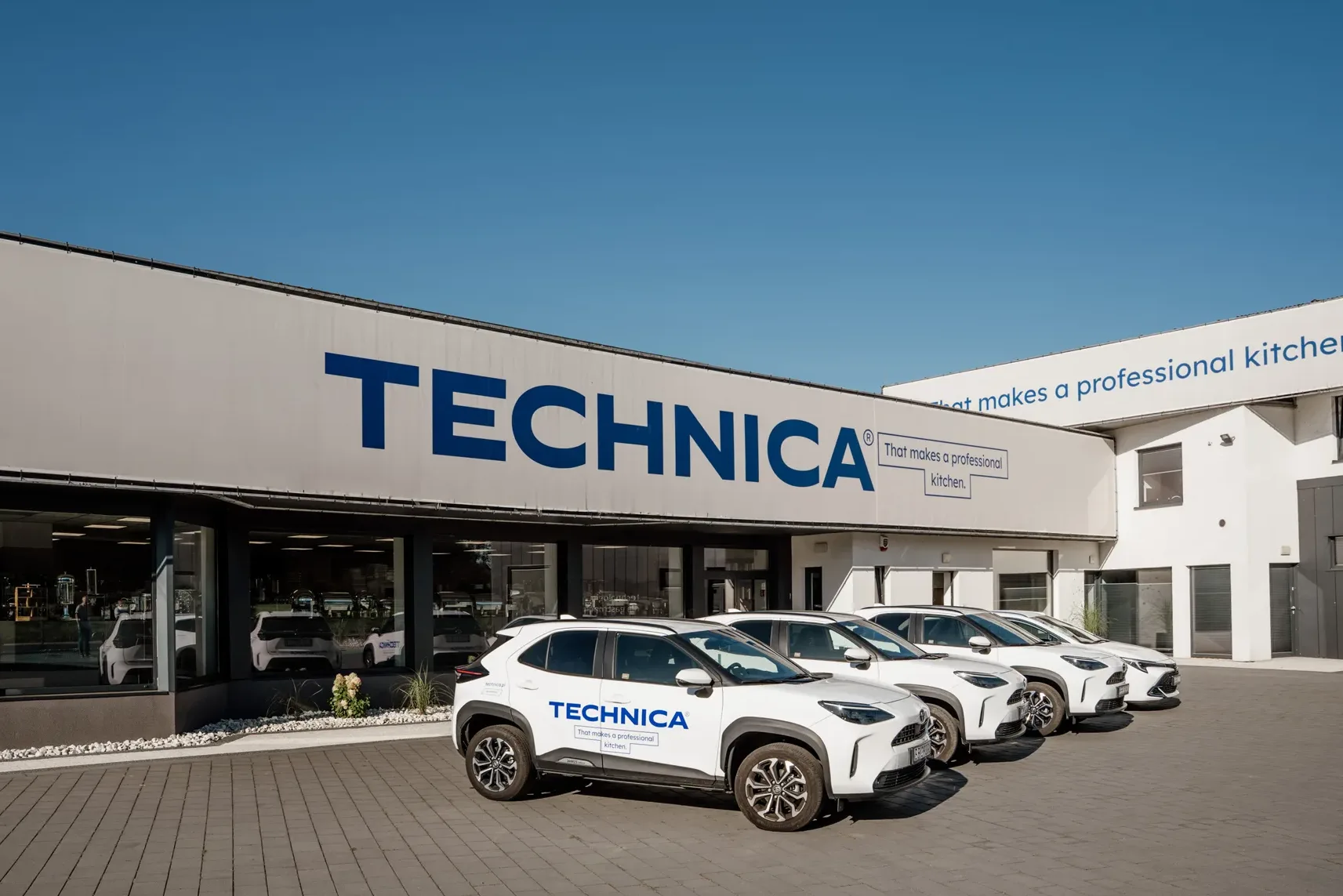 Siedziba firmy Technica – nowoczesny budynek biurowo-showroomowy z zaparkowanymi samochodami firmowymi oznaczonymi logo Technica.
