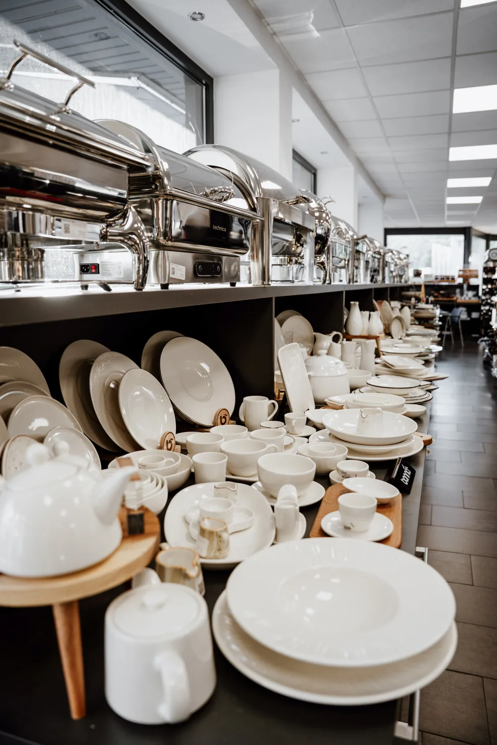Ekspozycja porcelany gastronomicznej i podgrzewaczy bufetowych w showroomie wyposażenia HoReCa, z widokiem na talerze, filiżanki i naczynia serwisowe.