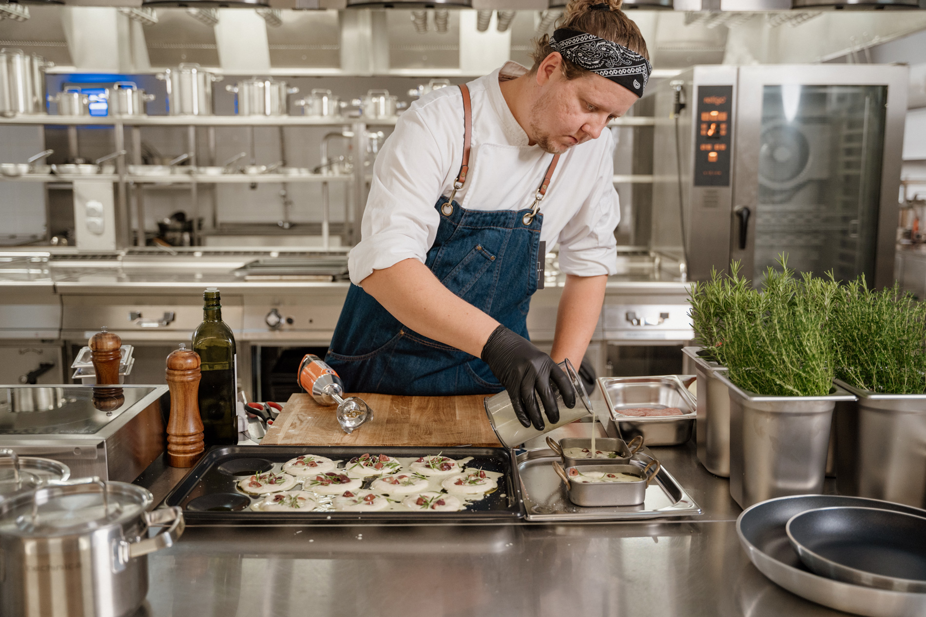 Szef kuchni przygotowujący danie w profesjonalnej kuchni gastronomicznej – precyzyjna praca na blacie ze stali nierdzewnej z użyciem naczyń i świeżych ziół.