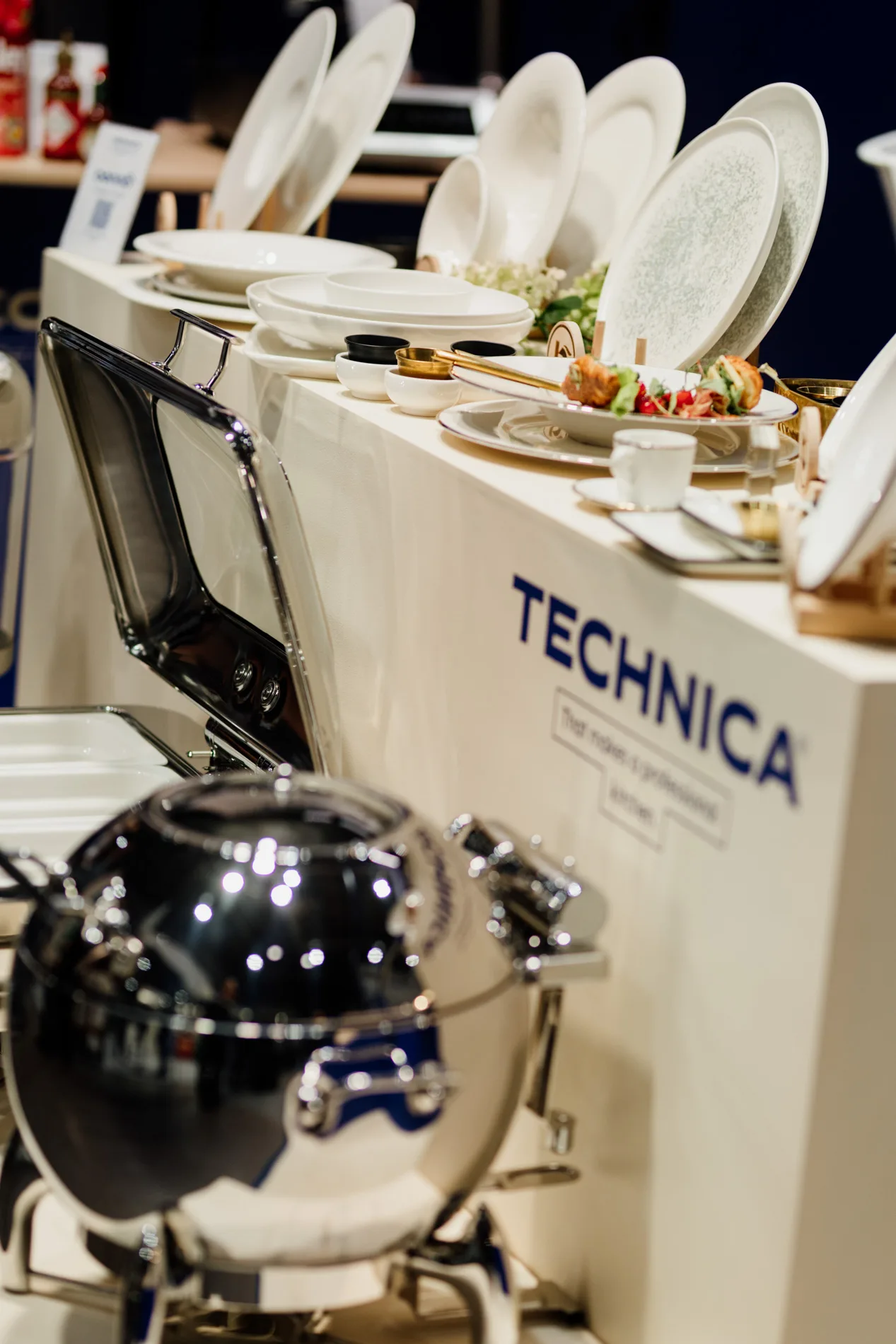 Ekspozycja porcelany i naczyń serwisowych na stoisku marki Technica, z aranżacją dań i profesjonalnym sprzętem gastronomicznym w tle.